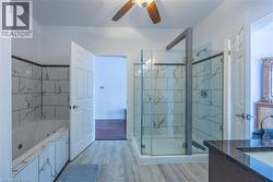 Contemporary bathroom featuring a glass-enclosed shower with tile surround, a built-in jetted tub with matching tile, wood-finish flooring, a ceiling fan, and a vanity with a dark countertop and integ - 