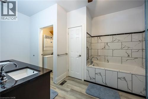 Bathroom featuring a built-in bathtub with subway tile surround, dark wood-finish vanity with an integrated sink and chrome faucet, and light wood-finish flooring - 514 Fishers Glen Road, Vittoria, ON - Indoor Photo Showing Bathroom