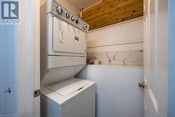 Dedicated laundry area with a stacked washer and dryer, wood-finish ceiling, and a white marble-patterned backsplash - 