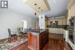 Gourmet kitchen featuring a central island with a dark countertop, extensive cream cabinetry, integrated stainless steel appliances, a tiled backsplash, and recessed lighting - 