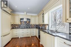 Kitchen featuring cream-colored cabinetry with decorative molding, dark countertops, and a mosaic tile backsplash - 