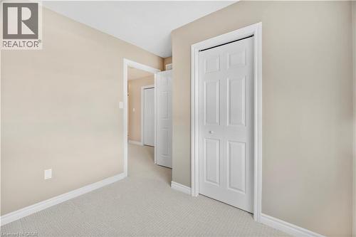 Hallway featuring light beige wall paint, white trim, light-colored carpet, and multiple six-panel bifold doors - 21 Davinci Boulevard, Hamilton, ON - Indoor Photo Showing Other Room