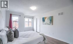 Bedroom featuring two windows with white trim, wood-finish flooring, white baseboards, and a white interior door - 