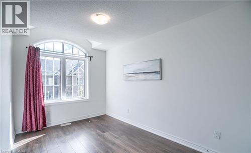 Room featuring a large arched window with multiple panes, dark wood-finish flooring, white baseboards, and a flush-mount ceiling light fixture - 14 Faye Street, Brampton, ON - Indoor Photo Showing Other Room