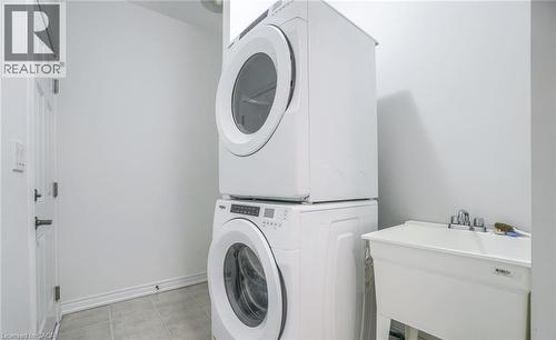 Laundry area featuring a stackable washer and dryer, a utility sink with a chrome faucet, white walls, and light-toned floor tiles - 14 Faye Street, Brampton, ON - Indoor Photo Showing Laundry Room
