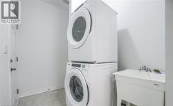 Laundry area featuring a stackable washer and dryer, a utility sink with a chrome faucet, white walls, and light-toned floor tiles - 