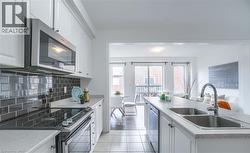 Kitchen featuring white cabinetry, a dark subway tile backsplash, stainless steel appliances, and a double basin sink - 