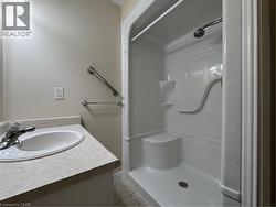 Bathroom featuring a white integrated sink vanity with a speckled countertop, a chrome faucet, a walk-in shower with a built-in seat, and stainless steel grab bars - 
