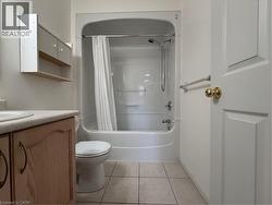 En-suite Four-piece Bathroom featuring a white tub/shower combination, light-colored floor tiles, and a vanity with wood-finish cabinetry - 