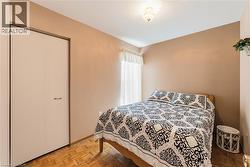 Neutral-toned bedroom featuring wood-finish parquet flooring, a window with sheer white curtains, and a flush-mount ceiling light - 