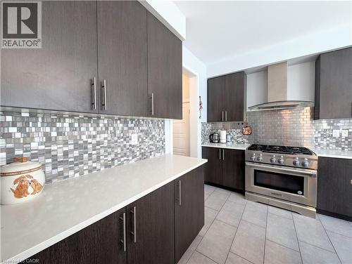Kitchen featuring dark wood-finish cabinetry, light-toned countertops, mixed-material mosaic tile backsplash, and a stainless steel range with a coordinating hood - 37 Mull Avenue, Caledonia, ON - Indoor Photo Showing Kitchen With Upgraded Kitchen