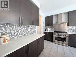 Kitchen featuring dark wood-finish cabinetry, light-toned countertops, mixed-material mosaic tile backsplash, and a stainless steel range with a coordinating hood - 