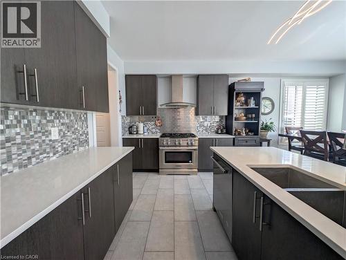 Contemporary kitchen featuring dark wood-finish cabinetry, light-toned countertops, a mosaic tile backsplash, stainless steel appliances, and a central island with an undermount sink - 37 Mull Avenue, Caledonia, ON - Indoor Photo Showing Kitchen With Double Sink With Upgraded Kitchen