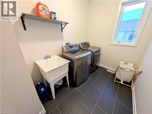 Functional laundry area featuring dark tile flooring, a utility sink, and a high-mounted window - 37 Mull Avenue, Caledonia, ON - Indoor Photo Showing Laundry Room
