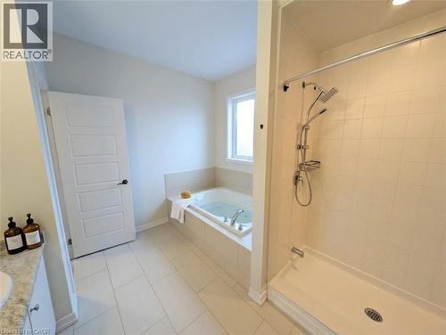Bathroom featuring a tiled walk-in shower with dual showerheads, a built-in jetted tub, a window above the tub, and light-toned floor tiling - 37 Mull Avenue, Caledonia, ON - Indoor Photo Showing Bathroom
