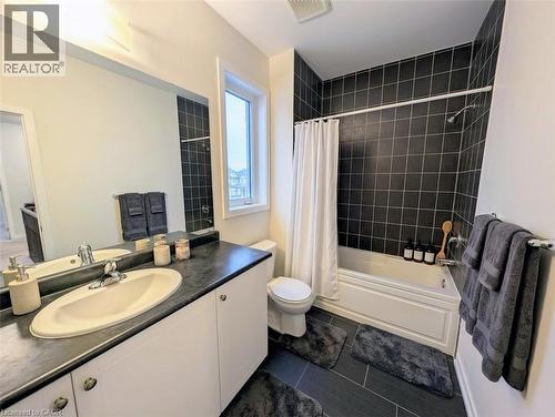 Bathroom featuring a white vanity with an integrated sink and dark countertop, large mirrored wall, and a window for natural light - 37 Mull Avenue, Caledonia, ON - Indoor Photo Showing Bathroom