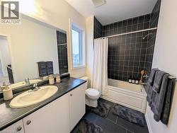 Bathroom featuring a white vanity with an integrated sink and dark countertop, large mirrored wall, and a window for natural light - 