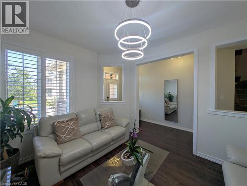 Living area featuring dark wood-finish flooring, white plantation shutters, and a three-tiered circular pendant light fixture - 37 Mull Avenue, Caledonia, ON - Indoor Photo Showing Living Room