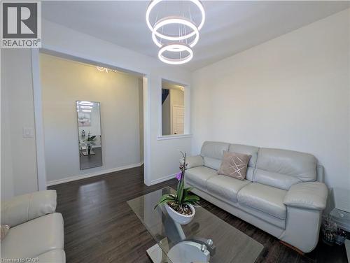 Living area featuring wood-finish flooring, a contemporary chandelier with circular rings, an open doorway, and a half-wall with a window-like opening - 37 Mull Avenue, Caledonia, ON - Indoor Photo Showing Living Room