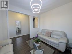Living area featuring wood-finish flooring, a contemporary chandelier with circular rings, an open doorway, and a half-wall with a window-like opening - 