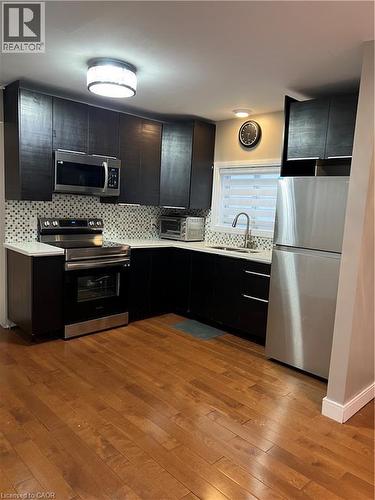 Kitchen featuring dark cabinetry, stainless steel appliances, a mosaic tile backsplash, light countertops, and wood-finish flooring - 179 S Vine Street S, St. Catharines, ON 