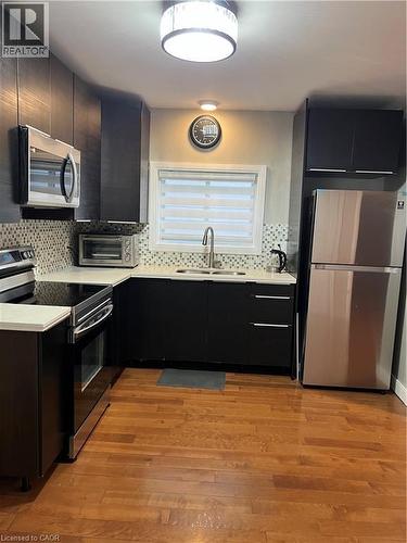 Contemporary kitchen featuring dark cabinetry, stainless steel appliances, and wood-finish flooring - 179 S Vine Street S, St. Catharines, ON 