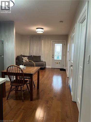 Wood-finish flooring extends throughout this open living space, featuring recessed and flush-mount lighting, a white entry door with decorative glass inserts, and a stainless steel refrigerator - 179 S Vine Street S, St. Catharines, ON 