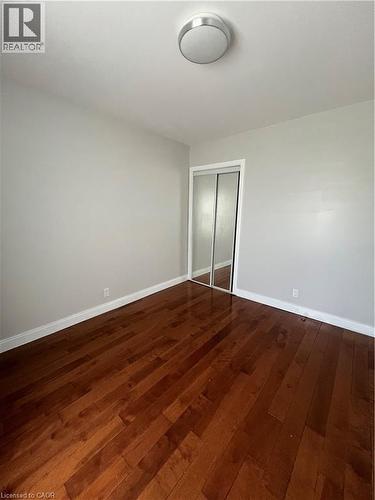 Rich wood-finish flooring provides a warm foundation for this room, featuring light gray walls, white baseboards, and a semi-flush mount ceiling light - 179 S Vine Street S, St. Catharines, ON 