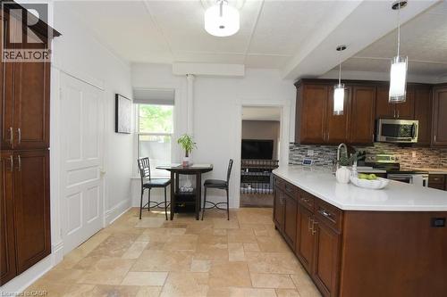 Kitchen featuring an expansive island with a light-toned countertop, rich wood-finish cabinetry, and a mosaic tile backsplash - 89 Lynden Road, Lynden, ON 
