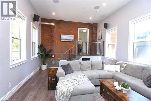 Family Room featuring an exposed brick wall, wood-finish flooring, recessed lighting, multiple windows, and an open stairwell with a dark wood railing - 89 Lynden Road, Lynden, ON 