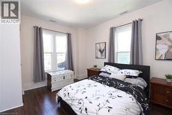 Bedroom featuring wood-finish flooring, two large windows, white baseboards, and a neutral wall color - 
