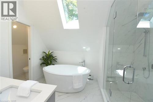 Modern bathroom featuring a water closet, freestanding soaking tub, a frameless glass shower with his and hers rain shower heads, double vanity, and skylight - 89 Lynden Road, Lynden, ON 