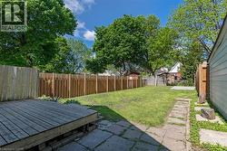 Expansive backyard featuring a wood deck, stone paver patio, a partial privacy fence, and mature perimeter trees - 
