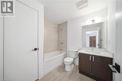 Bathroom featuring a white bathtub with tiled surround, a toilet, and a vanity with a white countertop and dark wood-finish cabinetry - 2782 Barton Street E Unit# 516, Hamilton, ON - Indoor Photo Showing Bathroom