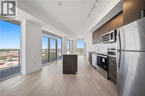 Open-concept living space featuring wood-finish flooring, a contemporary kitchen island with white countertop, dark wood-finish cabinetry, and stainless steel appliances - 2782 Barton Street E Unit# 516, Hamilton, ON - Indoor Photo Showing Kitchen