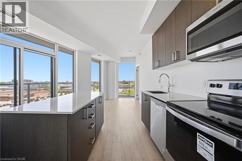 Contemporary kitchen featuring a full suite of stainless steel appliances, dark wood-finish cabinetry, and light-toned countertops - 2782 Barton Street E Unit# 516, Hamilton, ON - Indoor Photo Showing Kitchen With Upgraded Kitchen