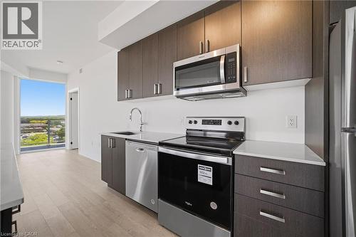Contemporary kitchen featuring dark wood-finish cabinetry, stainless steel appliances, and light-toned countertops - 2782 Barton Street E Unit# 516, Hamilton, ON - Indoor Photo Showing Kitchen With Upgraded Kitchen
