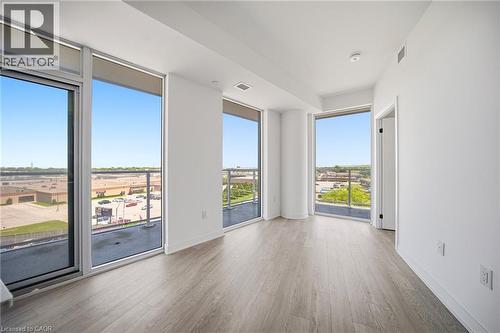 Bright interior space with expansive floor-to-ceiling windows, light wood-finish flooring, white walls, a balcony with a glass railing, and a modern ceiling light fixture - 2782 Barton Street E Unit# 516, Hamilton, ON - Indoor