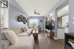 Open-concept living area featuring wood-finish flooring, a ceiling fan with integrated lighting, and a large window with blinds - 