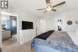 Carpeted bedroom featuring a ceiling fan with integrated lighting, an en-suite bathroom with a glass-enclosed shower, a single vanity with storage, and a mirrored closet door - 
