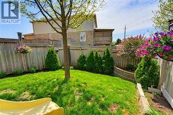Expansive backyard featuring a lush lawn, mature trees, wood fencing, and a terraced garden bed with a stone retaining wall - 