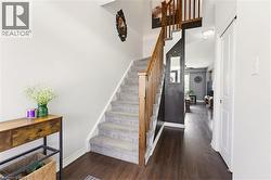 Welcoming entryway featuring dark wood-finish flooring, a carpeted staircase with wood railings, white baseboards, and a white interior door - 