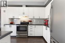 Modern kitchen featuring white cabinetry, dark countertops, a stainless steel range, a complementary stainless steel refrigerator, and wood-finish flooring - 