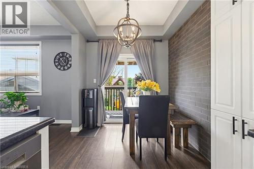 Dining area featuring wood-finish flooring, a tray ceiling with an overhead light fixture, a brick accent wall, and white built-in cabinetry with dark hardware - 100 Chester Drive Unit# 16, Cambridge, ON - Indoor Photo Showing Dining Room