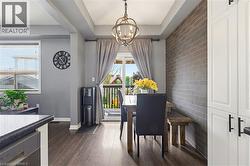 Dining area featuring wood-finish flooring, a tray ceiling with an overhead light fixture, a brick accent wall, and white built-in cabinetry with dark hardware - 