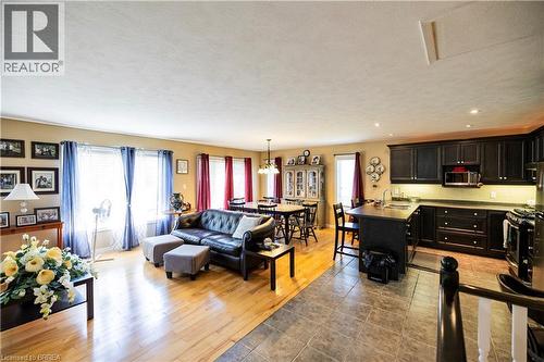 Open-concept living space featuring wood-finish flooring, a kitchen with dark cabinetry and stainless steel appliances, a central island with seating, recessed lighting, and a dining area with a chand - 100 Mechanic Street W, Waterford, ON - Indoor Photo Showing Other Room