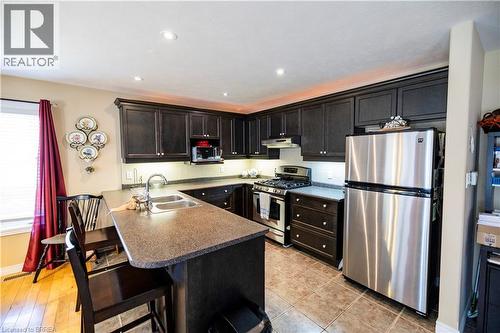 Kitchen featuring dark wood cabinetry, stainless steel appliances, a double basin sink, recessed lighting, and tile flooring - 100 Mechanic Street W, Waterford, ON - Indoor Photo Showing Kitchen With Stainless Steel Kitchen With Double Sink