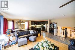 Open-concept living area featuring wood-finish flooring, a dining space with chandelier lighting, a kitchen with dark cabinetry and stainless steel appliances, and a tiled entryway - 