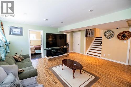 Finished lower level featuring wood-finish flooring, recessed lighting, a built-in media console, a staircase with dark treads, and a white interior door - 100 Mechanic Street W, Waterford, ON - Indoor Photo Showing Living Room