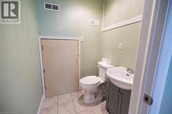 Bathroom featuring light green walls, white crown molding, a white toilet, a white porcelain sink, and a gray vanity cabinet - 